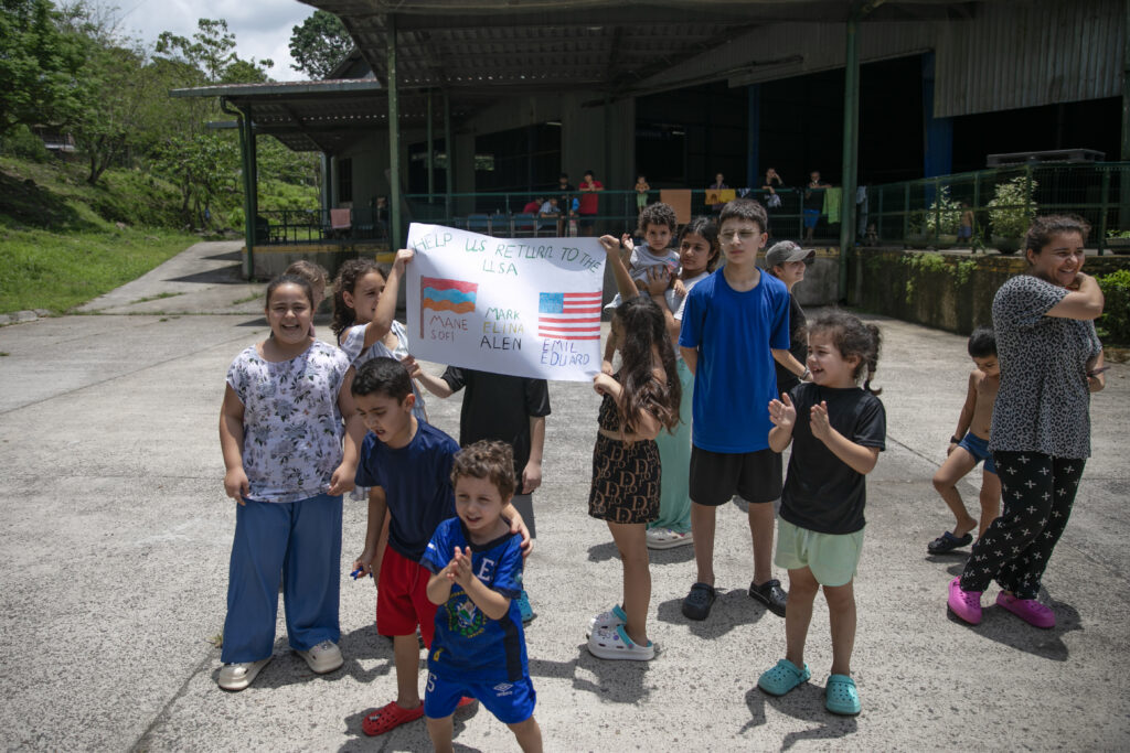 Un numeroso grupo de niños sostienen un cartel que pide ayuda para regresar a Estados Unidos| Foto: Galería News.